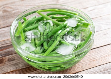 Green beans in a colander. Boiled or blanched vegetables in ice water on a wooden table