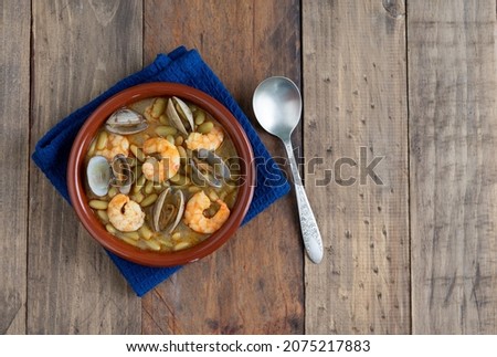 Green beans with prawns and clams in earthenware casserole on wood background. Copy space. top view.