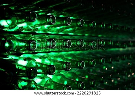 A lot of green beer bottles stacked on a wall, backlit in an interesting visual layout