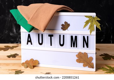 Green And Beige Hats In Cold Fall Weather. Autumn Inscription On Lightbox. Advertising Template