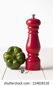 Green Bell Pepper And Red Pepper Grinder On White Wooden Table