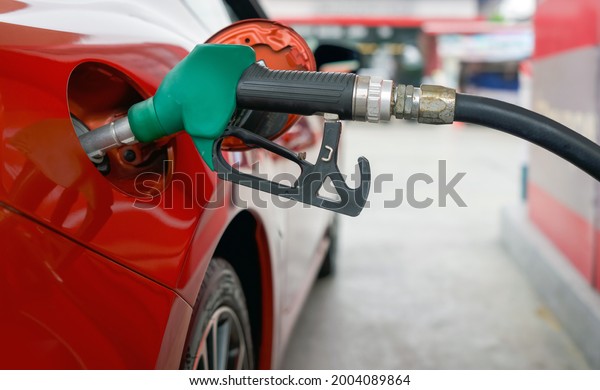 Green benzene gas pump nozzle filling up red sport car\
tank. Close up