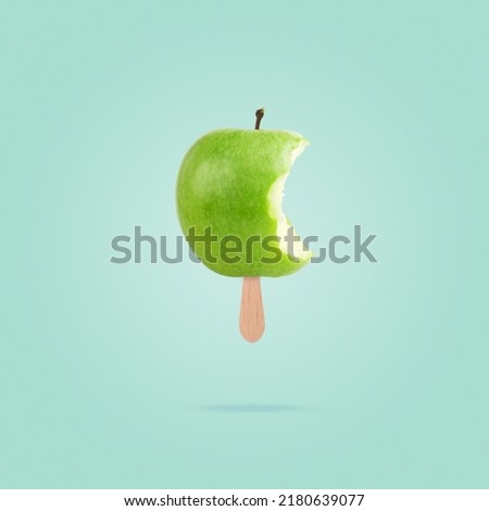 Green bitten apple with ice cream stick on pastel blue background. Diet healthy concept. Creative summer concept.