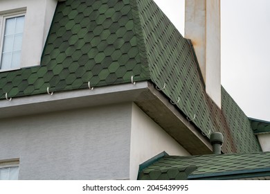 Green bitumen roof of house under construction with smokestack and holders for gutters water drainage system. Cottage roof with slopes and chimney. Flexible bitumen or slate shingles