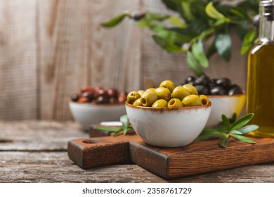 Aceitunas verdes, negras y rojas, aceite de oliva sobre un fondo de madera marrón. Aceitunas jugosas frescas en un bol y hojas de oliva frescas. Vegan. Frutas de oliva. Colocar el texto. Copiar espacio.