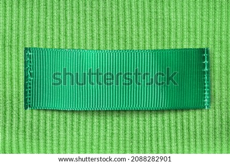 Green blank clothing label sewn on green knit background closeup