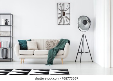 Green blanket on beige settee in bright living room with lamp and clock on white wall with copy space - Shutterstock ID 768773569