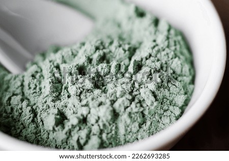 Green (blue) bentonite facial clay (alginate mask, body wrap) in a bowl. Clay texture close-up, selective focus.