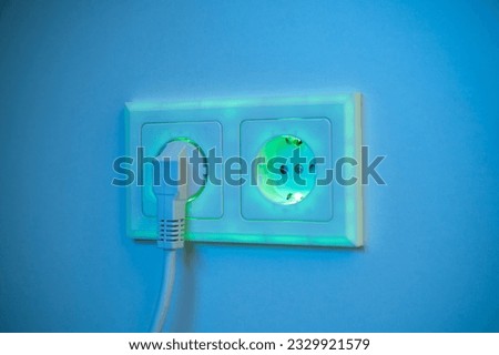Green and blue illuminated socket with plug inserted to symbolise power consumption and electrical energy from a socket outlet providing green and clean energy