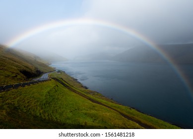 The green and blue landscape being brightened up by a colorful rainbow arc and sunlight breaking through the clouds and mist. 