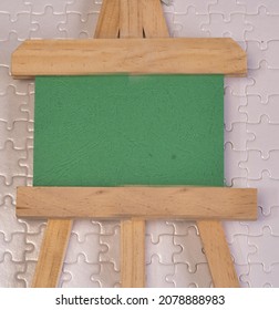 A Green Board On Wooden Easel With White Puzzle Board As Background. Copy Space For Add-on.