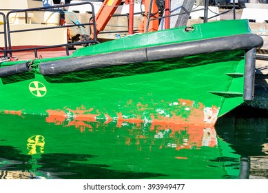 A Green Boat Keel With Black Rubber Bumpers In Reflective Water.