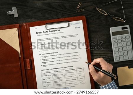 Green Bond Framework: Realistic mock-up mock placed on with calculator, pen. Contributor-created fictional business document for illustrative purposes.