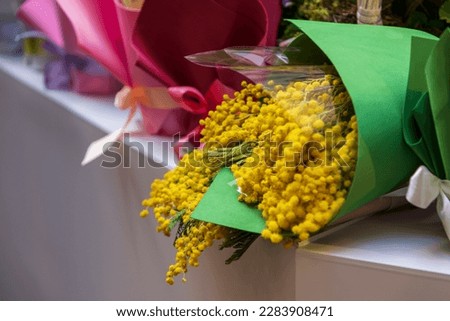 Green bouquet with yellow fresh cut Acacia Dealbata (also known as silver wattle or mimosa) flowers stands in florist shop. Soft focus. Copy space. Flower business theme.