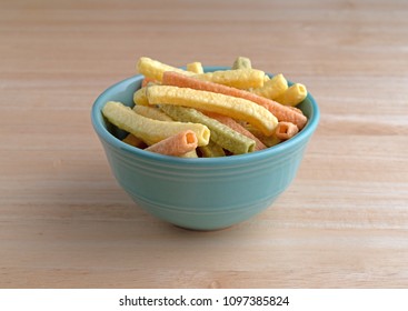 A green bowl filled veggie straws on a wood table.