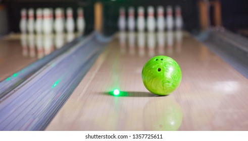 Green Bowling Ball Put On Alley With Blurred Bowling Pin Background