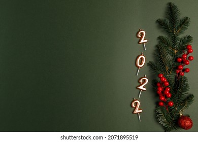 Green branches of a Christmas tree and red berries, candles numbers 2022, Christmas decor on a green background. Place for text, Christmas postcard.