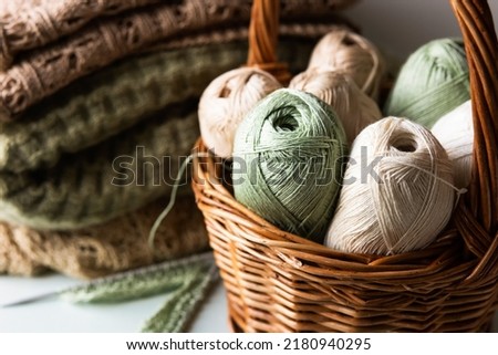 Green and brown yarn threads in a basket for knitting warm clothes with knitting needles and finished yarn products, knitting hobby