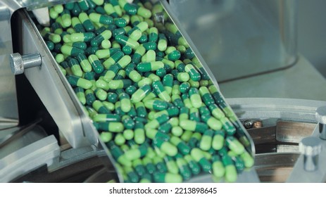 Green Capsules Move Along The Metal Automatic Conveyor, Fall Into The Drum For Sorting And Preparation For Packaging. Medicine Production Line In Pharmaceutical Factory. Pharma Company