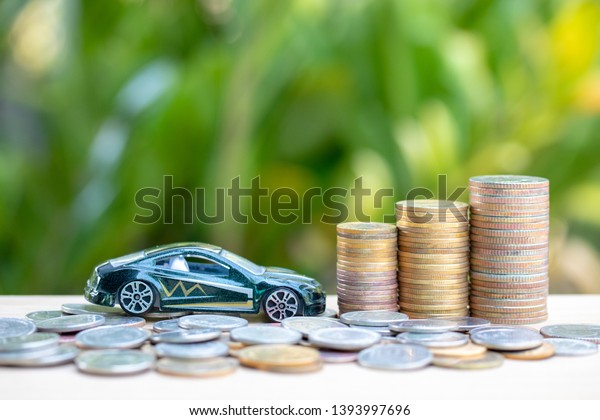 green car and coins\
or money on wooden in a tree background.Concept car makes money or\
saving money for car.
