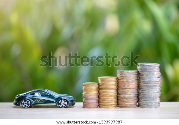 green car and coins\
or money on wooden in a tree background.Concept car makes money or\
saving money for car.