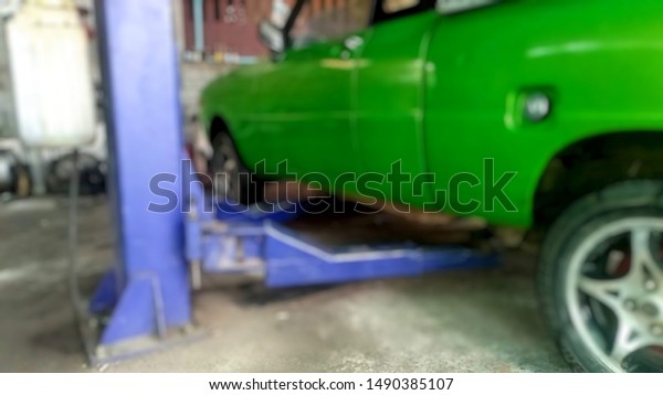 The green car was parked on the car lift equipment\
to lift it up and check the underside, continue maintenance ...\
lens blur
