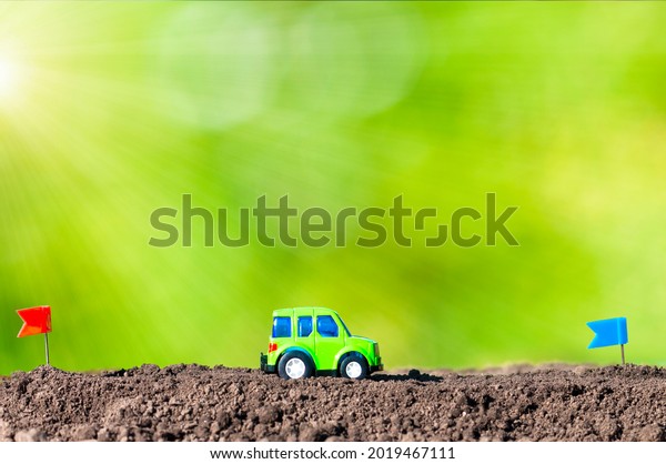 a green car rides on the\
ground in the rays of the sun from the red flag start to the blue\
flag finish, the concept of traveling by car, driving along the\
route