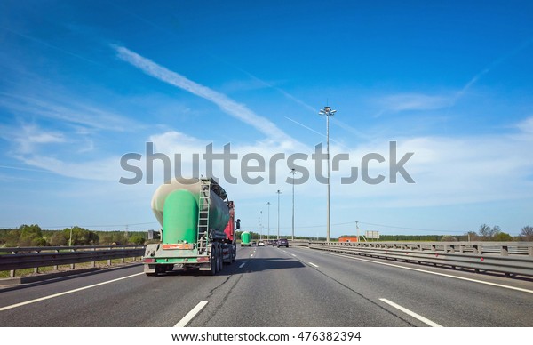 Green cargo tanker truck goes on asphalt highway\
under blue sky, rear view