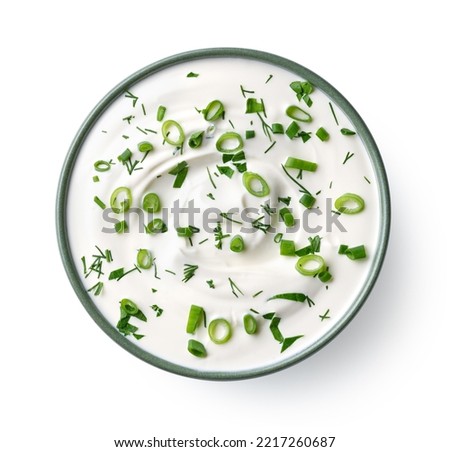 Green ceramic bowl of sour cream dip sauce with fresh herbs isolated on white background, top view