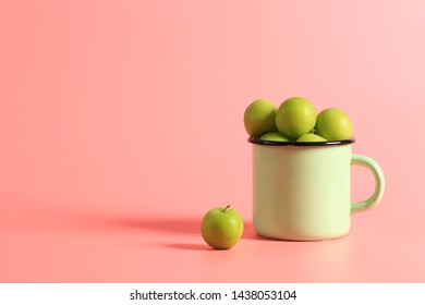 Green Cherry Plum In An Enamel Mug On A Pink Background. Creative Minimalist Style. Healthy Food