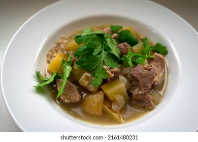 Green Chili Pork Stew With Potatoes, Cilantro And Onion Served In A White Flat Bowl