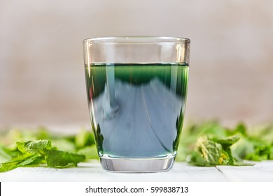 Green chlorophyll drink in glass with water on white table with green mint