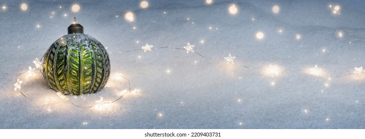 Green Christmas Ball With Shiny String Lights In White Deep Snow, Wintry Xmas Decoration Background With Copy Space For Greeting Card In December Holiday Season