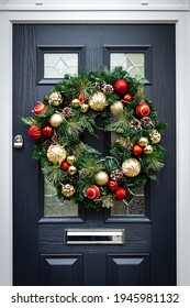 Green Christmas Wreath with red and golden balls on a black wooden front door