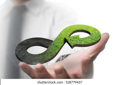 Green circular economy concept. Hand showing arrow infinity symbol with grass texture.