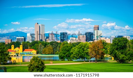 Green City Park View of Denver Colorado downtown skyline rising behind green city park tree line with Rocky Mountain background wide panoramic view 