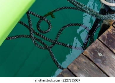 green clear water in which there is a large braided green rope connecting the boardwalk and the side of the boat