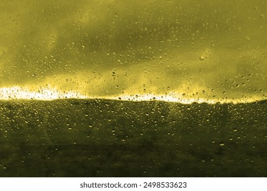 Green cloudscape, view of the landscape through the wet window, drops on the glass, rainy scene, cold weather, dark horizon and heaven with clouds, outside, colored photo