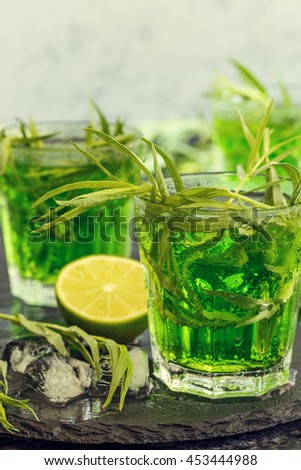 Green cocktail with lime, soda, crushed ice and tarragon leaves, black background, selective focus.