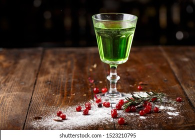 green cocktail on the basis of absinthe in a stylish vintage glass on a brown wooden background. white sugar and cranberries are scattered nearby