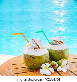 Green coconuts and flower on wood table at swimming pool in summer.