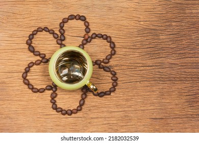A green coffee cup surrounded by coffee beans is placed in the shape of a flower on a wooden table.
