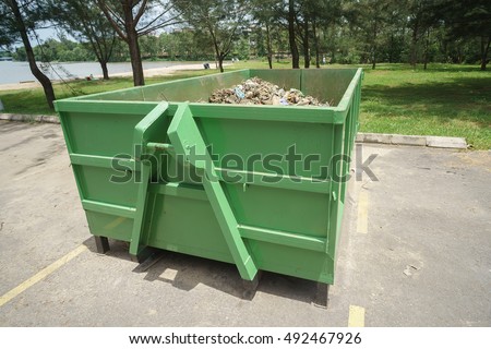 Green colored dump bin at open space parking area.