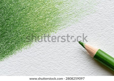 A green colored pencil creates a gradient of green hues on a textured white paper surface, showcasing the art of color blending.