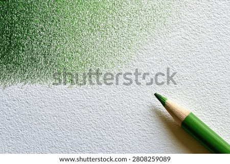 A green colored pencil is shown in the foreground, with a textured area of green shading on white paper in the background.