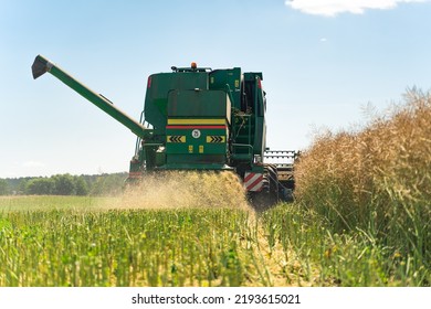 Green combine harvester watering the rapeseed field after harvesting. Back view from the ground perspective. Beautiful weather. High quality photo