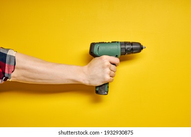 Green cordless battery powered drill on yellow background, cropped male hands holding tool for repair and building construction. copy space for advertisement - Shutterstock ID 1932930875