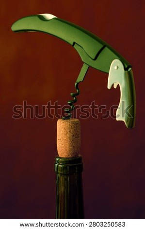 Green corkscrew opener pulling cork from dark wine bottle neck. Sommelier tool close up on dark background.