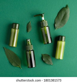 Green Cosmetic Bottles With Plant Leaves On Green Background. SPA Natural Organic Beauty Products, Packaging Without Labels For Branding Mockup. Flat Lay, Top View.