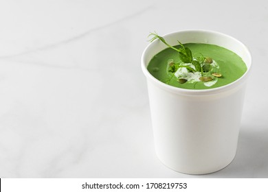 Green cream soup in paper package or disposable cup with pea and spirulina. Vegan food delivery concept. mock up